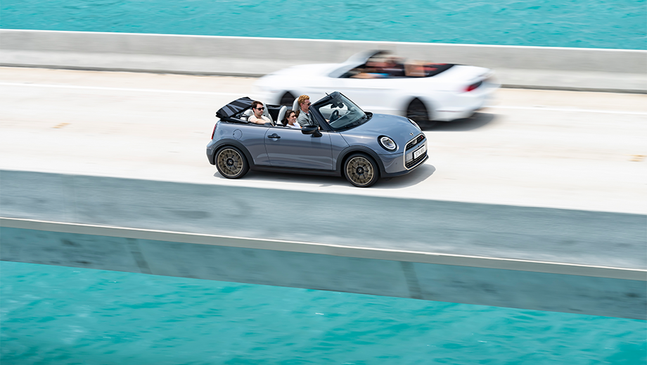 Side view of a Mini Cooper S Convertible with the top down on a bridge over water