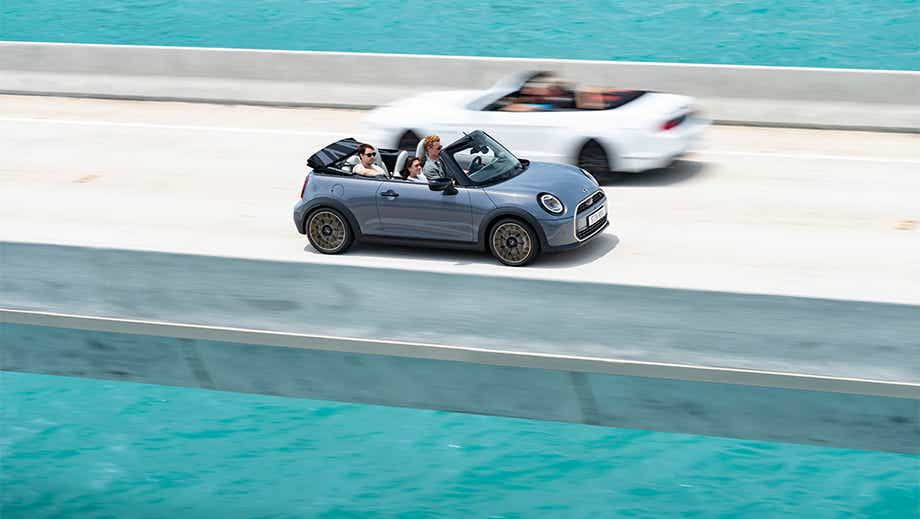 Side view of a Mini Cooper S Convertible with the top down on a bridge over water