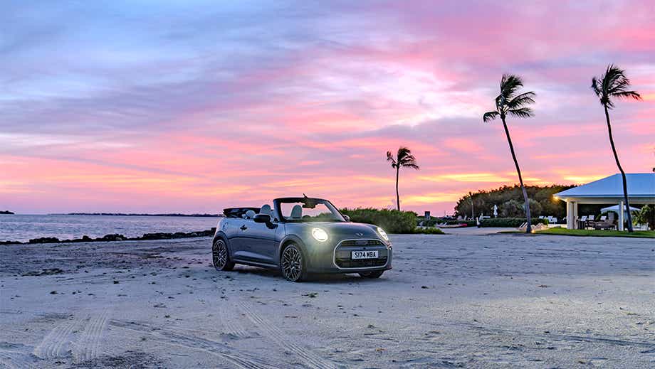 Front three quarter of a Mini Cooper S Convertible on a beach at sunset