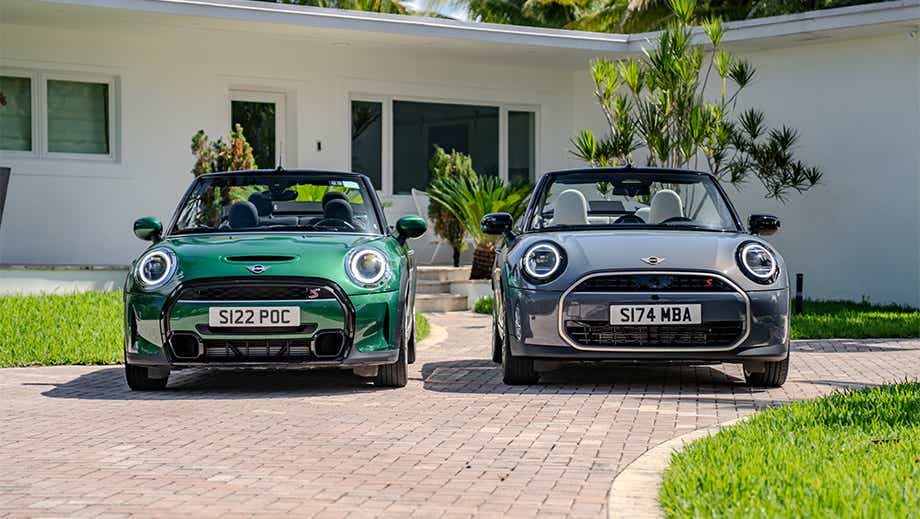 Front view of a british racing green mini cooper s convertible and another mini cooper s convertible parked in front of a house