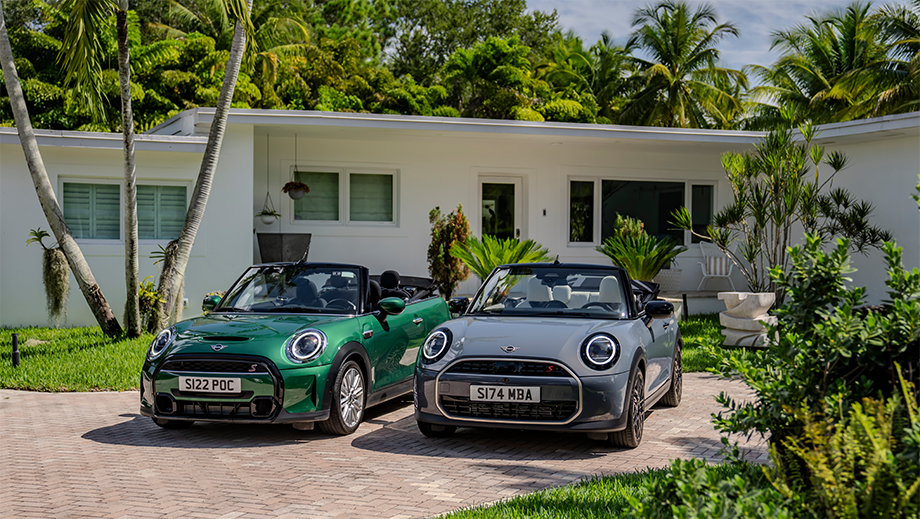 Front view of a british racing green mini cooper s convertible and another mini cooper s convertible parked outside a house
