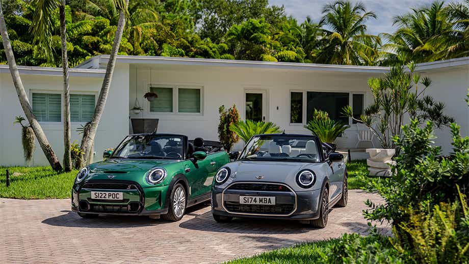 Front view of a british racing green mini cooper s convertible and another mini cooper s convertible parked outside a house