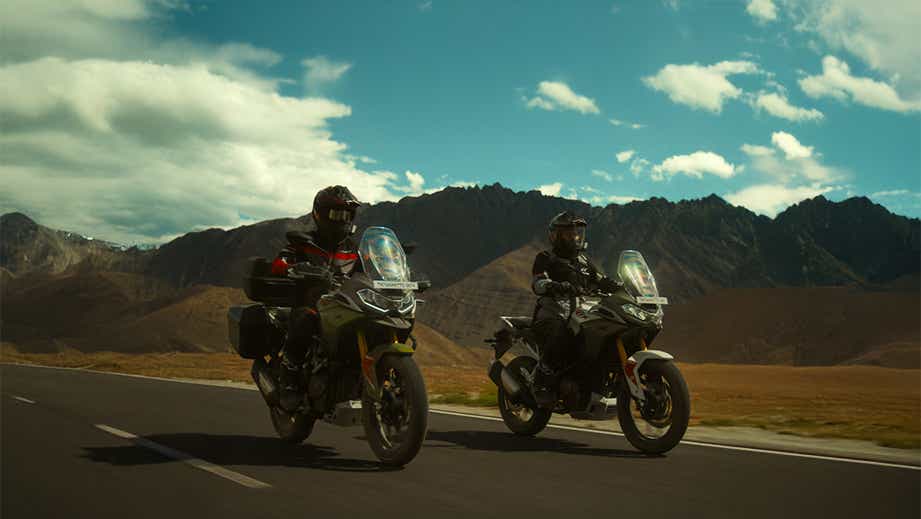 Action road view of a TVS Apache RTX with riders against mountain landscape
