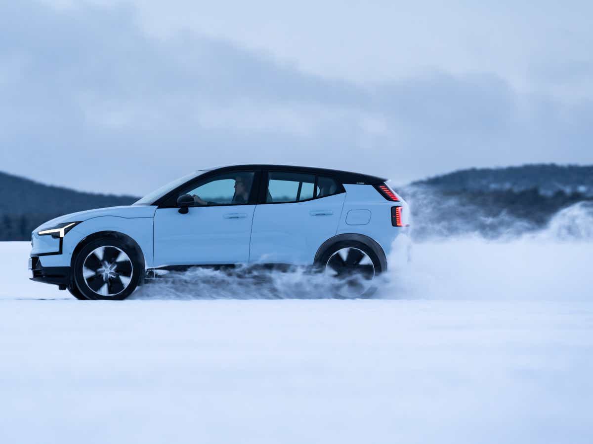 Side view of a cold blue Volvo EX30 driving on snow